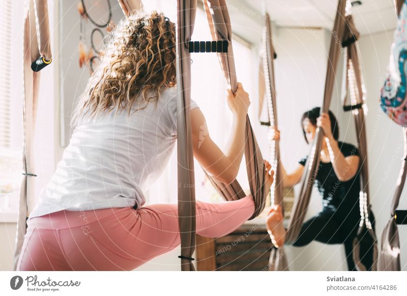 Ein Mädchen mit lockigem Haar praktiziert Yoga mit einer Hängematte. Yoga, Aero Yoga, Fitness, Lifestyle. Rückansicht Antenne Frau jung Antigravitation Asana