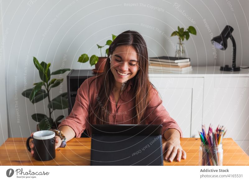 Lächelnde Frau mit Ohrstöpseln beim Tippen auf dem Laptop zu Hause Arbeitsplatz Netbook Glück Browsen Zahnfarbenes Lächeln zufrieden benutzend heiter klug