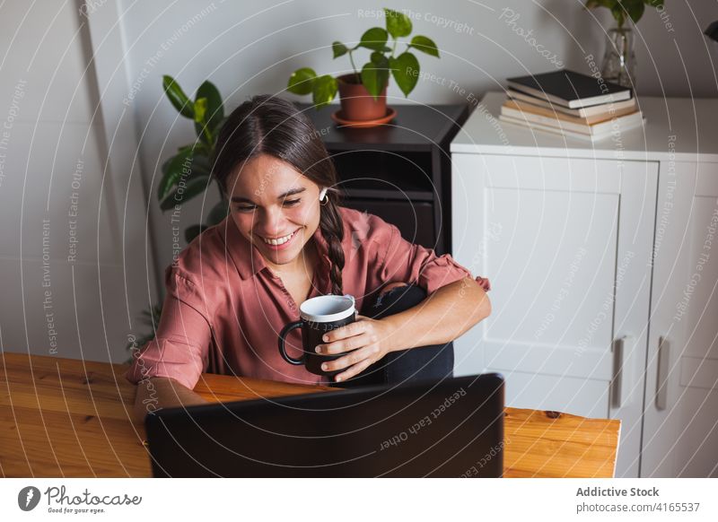 Gut gelaunte Frau mit einer Tasse Kaffee am Laptop Netbook Glück Browsen Zahnfarbenes Lächeln benutzend heiter klug zuschauen Surfen Apparatur Zeitgenosse