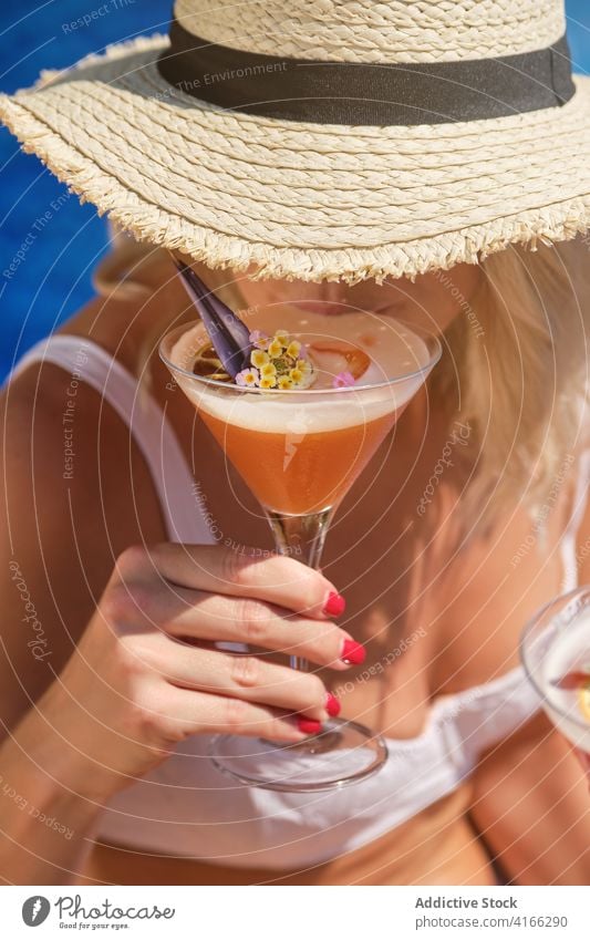 Unbekannte Blondine trinkt erfrischenden Cocktail am Pool Frau trinken Beckenrand Feiertag Erfrischung Reisender Stil Mode sich[Akk] entspannen exotisch