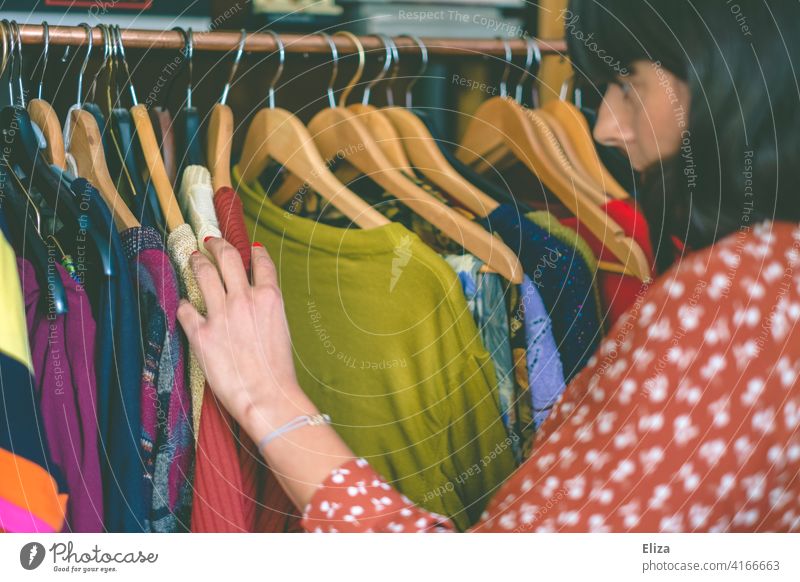 Junge Frau stöbert durch Klamotten auf einer Kleiderstange im Second Hand Laden oder auf dem Flohmarkt. Kleidung stöbern Anziehsachen bunt shopping
