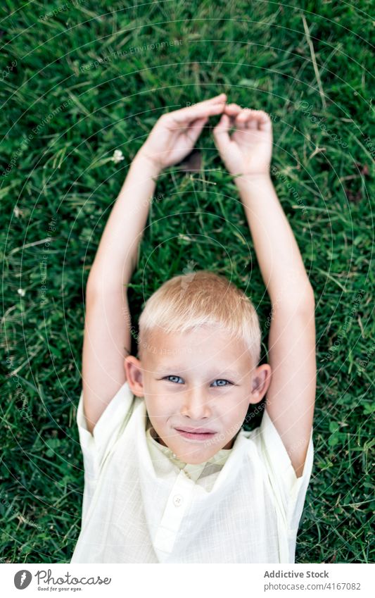 Glücklicher Junge, der sich bei Tageslicht auf dem Rasen ausruht Kind Gras Kälte Wochenende ruhen Vergnügen Hand hinter dem Kopf sich[Akk] entspannen heiter