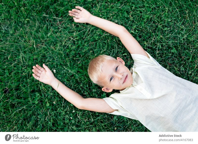 Glücklicher Junge, der sich bei Tageslicht auf dem Rasen ausruht Kind Gras Kälte Wochenende ruhen Vergnügen Hand hinter dem Kopf sich[Akk] entspannen heiter
