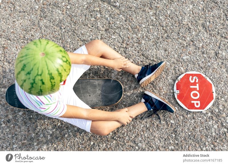 Junge in dekorativer Kopfbedeckung mit Schild auf der Fahrbahn stoppen verbieten Einschränkung trendy Skateboard Straße Wassermelone Kind Sommer lässig Streifen