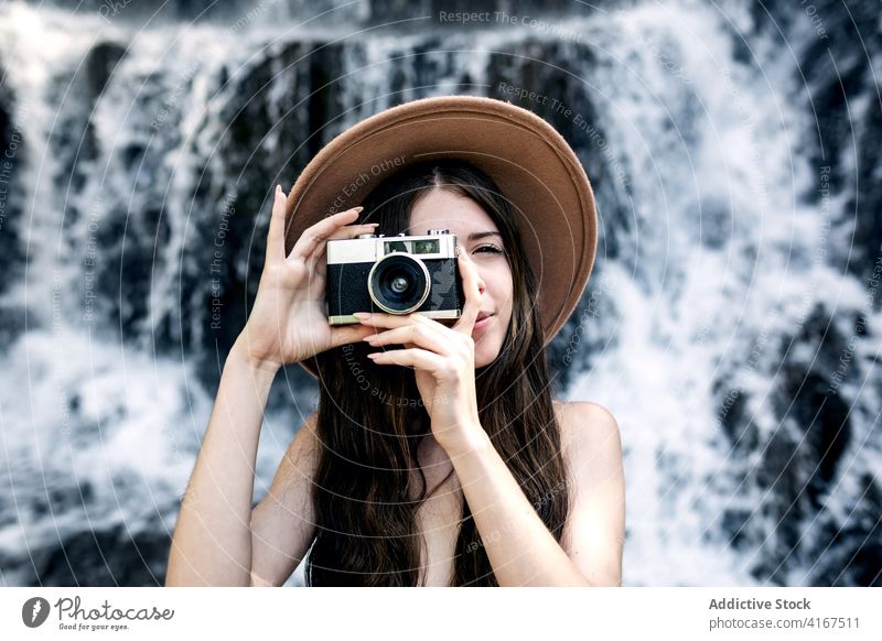 Stilvolle Frau, die mit einer alten Kamera fotografiert altehrwürdig Fotoapparat Reisender fotografieren retro altmodisch Wasser Natur Wasserfall Urlaub Hut