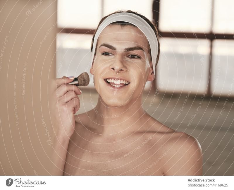 Hemdloser junger Mann beim Schminken bewerben Make-up androgyn Atelier Fundament Bürste Transgender ohne Hemd Spiegel männlich queer Wange Kosmetik Stirnband