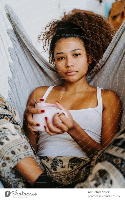Ethnische Frau mit Tasse Kaffee ruht in Hängematte zu Hause ruhen trinken sich[Akk] entspannen Kälte gemütlich jung Afroamerikaner schwarz ethnisch Getränk