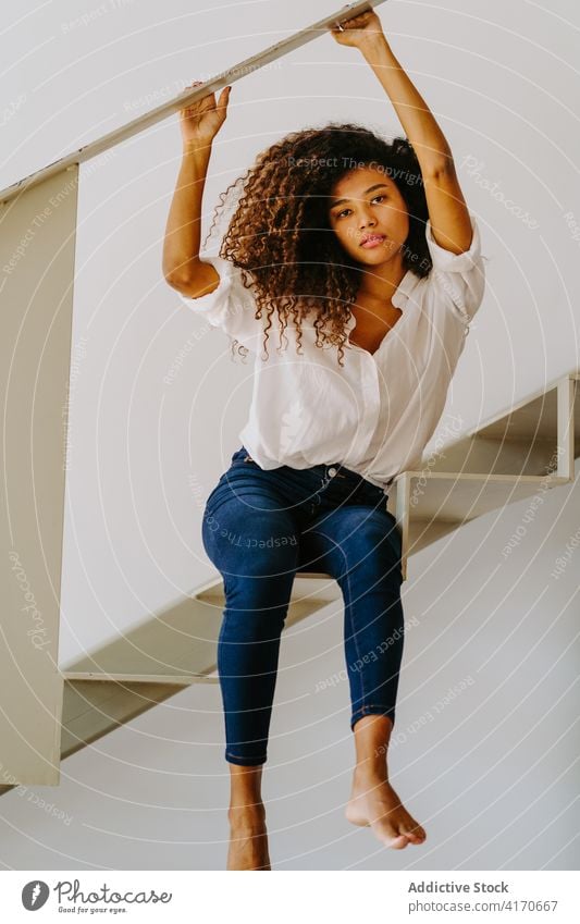 Ethnische lockig behaarte Frau sitzt auf einer Treppe Stil trendy Frisur Afro-Look krause Haare Barfuß modern attraktiv jung ethnisch lange Haare Mode Lifestyle