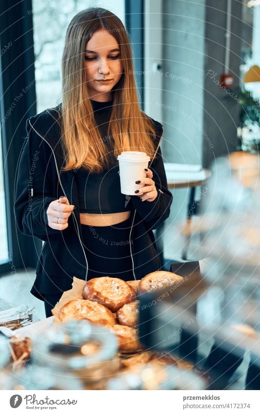 Frau hält Tasse mit Kaffee Blick auf Gebäck, Brötchen, Kuchen und Kekse und wartet auf die Bestellung. Mädchen kauft ein süßes Essen und heißes Getränk zum Mitnehmen. Junge Frau mit einer Pause beim Einkaufen in einem Café