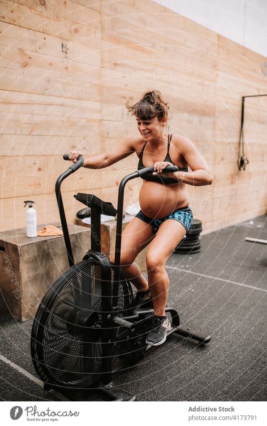 Schwangere Frau bei Übungen auf dem Airbike im Sportzentrum Fahrrad schwanger Sportlerin Fitnessstudio Zyklus Maschine Herz operativ Training Athlet physisch