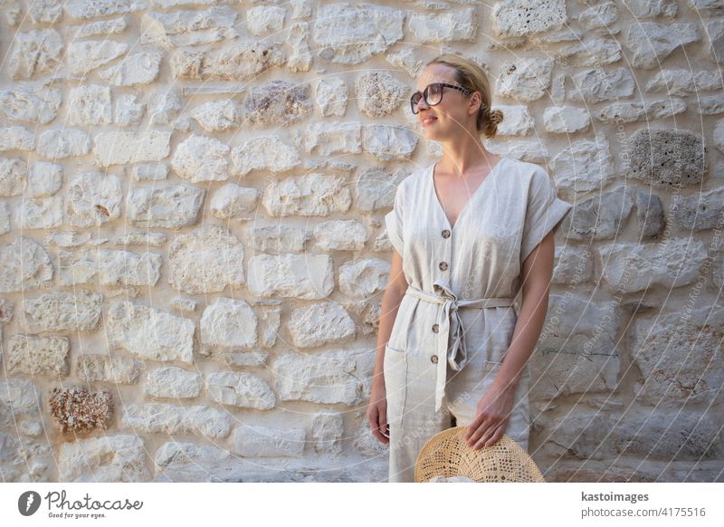Porträt der schönen fröhlichen blonde Frau trägt ein Stück Sommerkleid und Sommerhut, stehend vor der alten mittelalterlichen Steinmauer. Sommerurlaub Porträt Konzept. Kopieren Raum.
