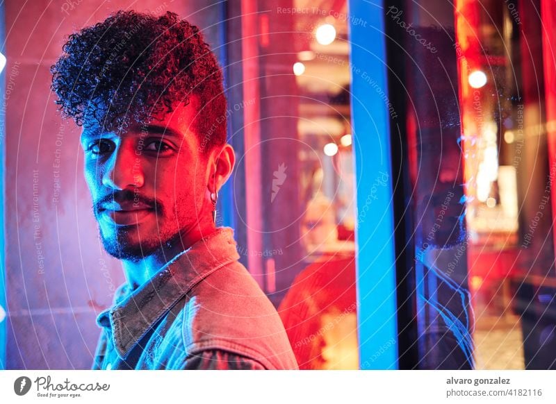 junger hispanischer Mann in der Nähe eines Neonlichts mit blauen und roten Lichtern neonfarbig männlich Model Erwachsener Menschen Person Porträt Typ Gesicht