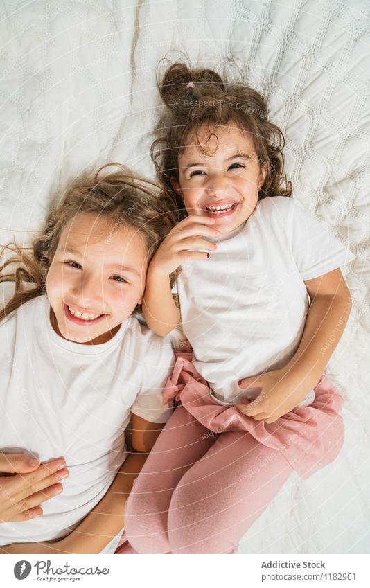 Fröhliche Schwestern liegen auf einem gemütlichen Bett und schauen in die Kamera Mädchen aufgeregt Spaß haben Freude heiter Glück Geschwisterkind Energie