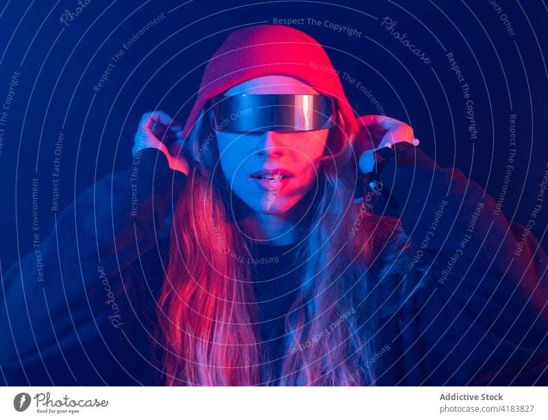 Stilvolle junge Dame mit trendiger Sonnenbrille steht in einem dunklen Raum mit Neonröhren Frau neonfarbig selbstsicher Vorschein Mode futuristisch informell