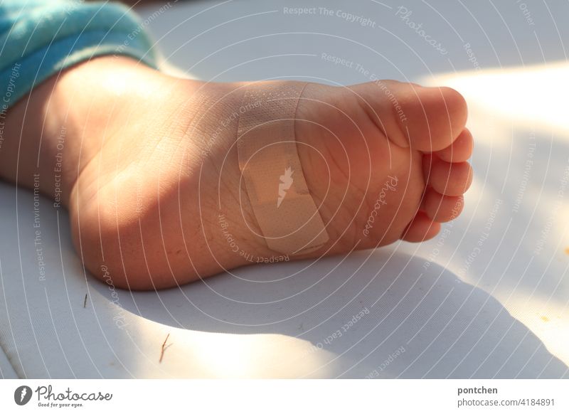 ein Fuß mit Pflaster liegt in der Sonne. Kleinkind- Verletzung und Heilung pflaster verletzung trost heilung fuß kleinkind behüten schutz fürsorge kindswohl