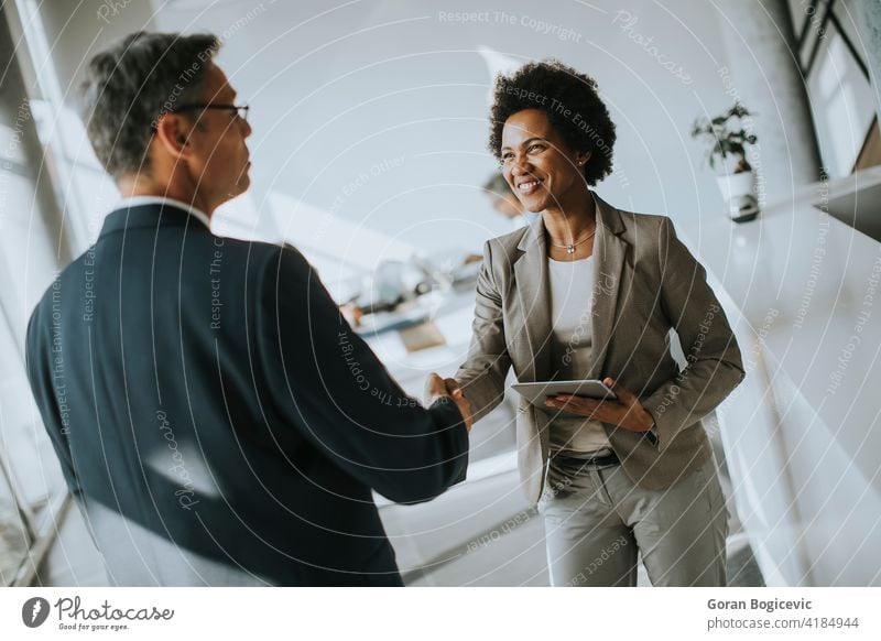 Geschäftsfrau hält digitale Tablette und Blick auf gut aussehende Kollegen beim Händeschütteln im Büro Glück Lächeln Exekutive Arbeiter Geschäftsmann ethnisch