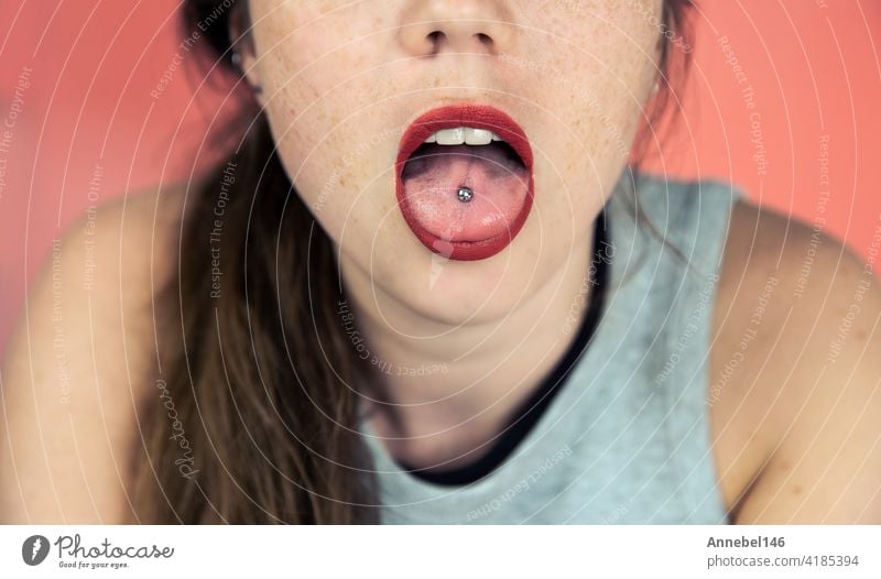 Close up Porträt der jungen Frau mit Sommersprossen sticking out gepiercte Zunge, zeigt ihre Zunge Piercing mit rosa Hintergrund Mode Person Mädchen erotisch