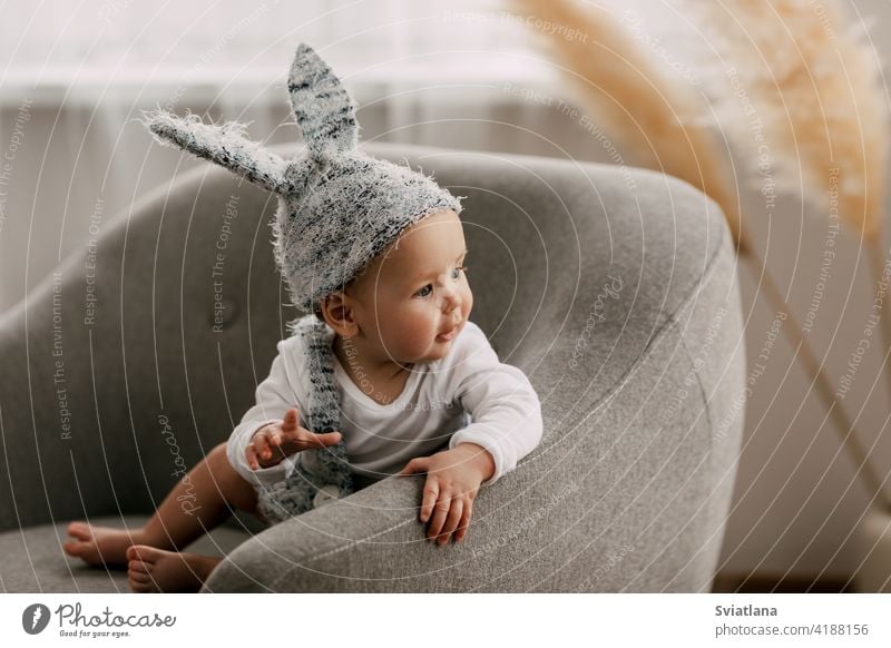 Kind in lustigen Osterhase Kostüm sitzt auf einem Stuhl und lacht Baby Kaninchen Anzug Ostereier Spiel Sitzen Spielzeug Bett Innenbereich Lachen schlafen