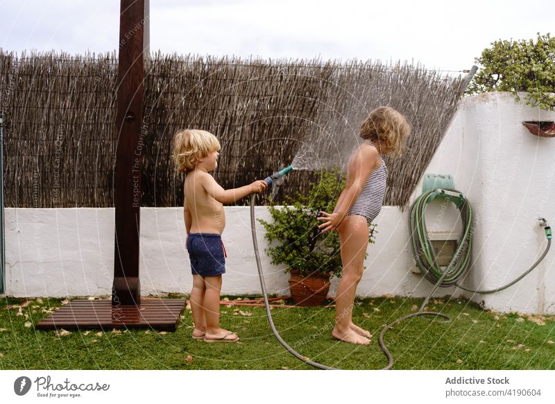 Bezaubernde kleine Geschwister spielen mit Wasserschlauch im Hinterhof Kinder Hof Schlauch Spaß haben eingießen Zusammensein Geschwisterkind Kindheit Glück