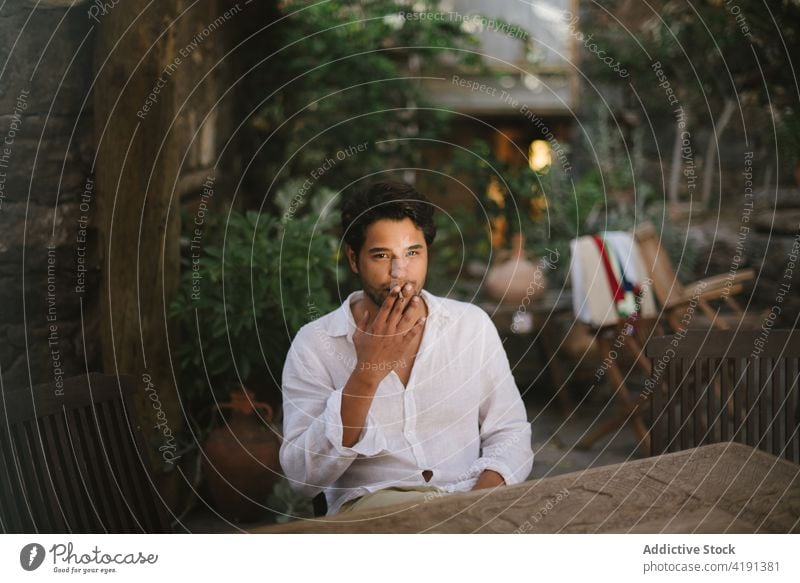 Junger dunkelhaariger Junge raucht eine Zigarre, während er auf einer Veranda sitzt Mann Kaukasier Sitzen männlich Person Rauch Rauchen Zigarette gutaussehend