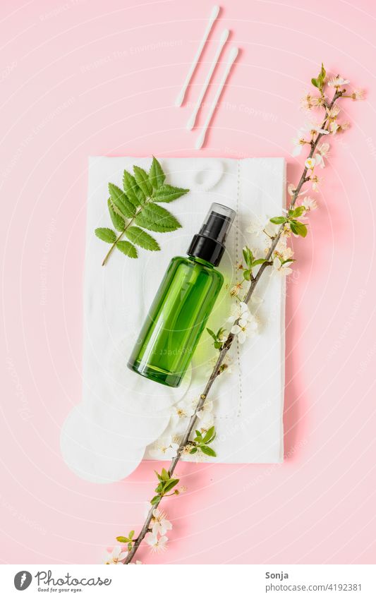 Eine grüne Parfüm Flasche und Kosmetikartikeln auf einem rosa Hintergrund. Flatl lay. Frühling. Kosmetikprodukte Wattestäbchen Wattepads Blütenpflanze flatlay