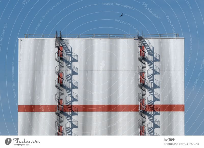 zwei Wendeltreppen mit Rabenvogel und Schattenwurf an einem großen Lagerhaus Symmetrie Präzision Ordnung Design elegant weiß rot modern Industrieanlage