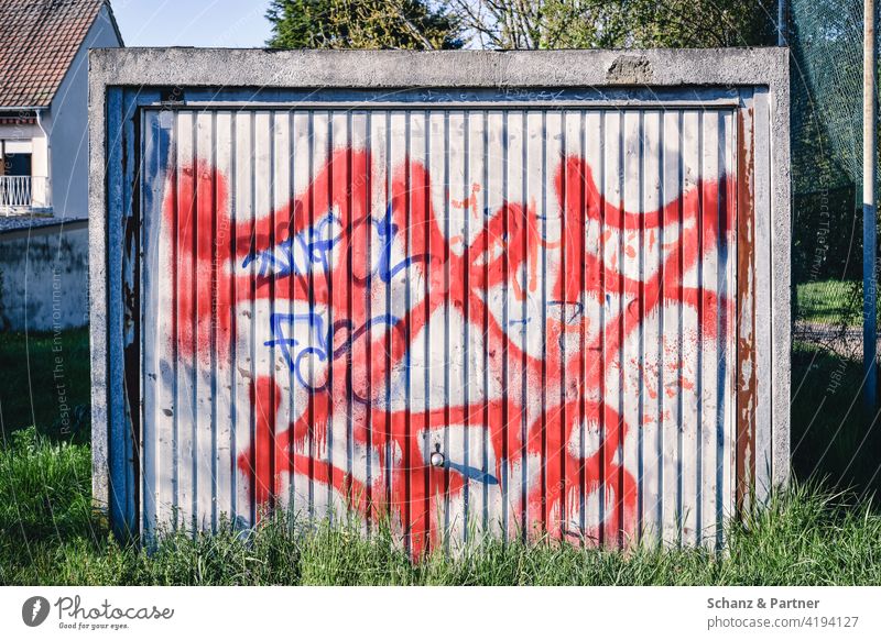 mit Graffiti besprühtes Garagentor einer Fertiggarage Eingang rot zugewachsen Beton Tags Blech vergessen verwittert Geheimnis Tor geschlossen Einfahrt verrostet