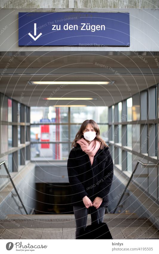 Eine junge Frau mit FFP2 - Maske steht am Bahnhof vor der Treppe zu den Gleisen, Zügen. Maskenpflicht Deutsche Bundesbahn DB Pandemie covid-19 Coronavirus