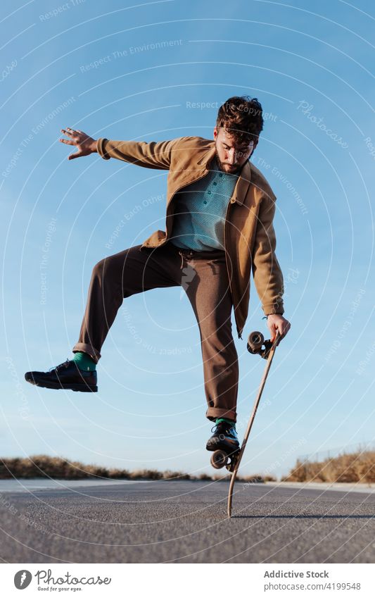 Trendiger Skater, der auf dem Skateboard stehend das Gleichgewicht hält Mann Trick Natur ausführen Saum Fähigkeit Landschaft ländlich Hobby Straße männlich