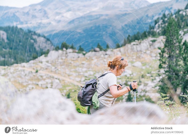 Aktive Frau, die mit Stöcken auf einem steinigen Berghang spazieren geht Spaziergang Stangengehen aktiv Hügel Weg Energie Trekking Nordic Walking physisch