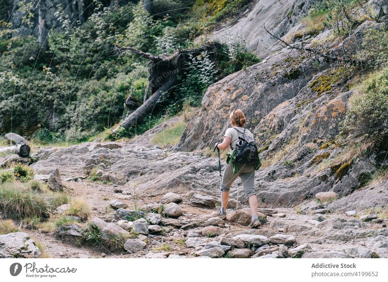 Anonyme aktive Frau, die mit Stöcken auf einem steinigen Berghang spazieren geht Spaziergang Stangengehen Hügel Weg Energie Trekking Nordic Walking physisch