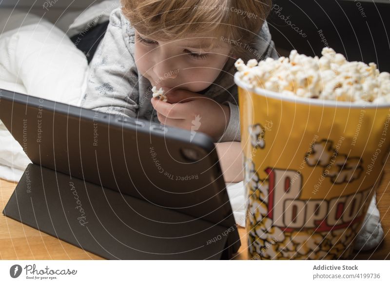 Kind auf der Couch, das auf dem Tablet fernsieht und Popcorn isst Junge genießen Filmmaterial Tablette Liege Spaß haben Cartoons Lifestyle Sofa Kinder Snack