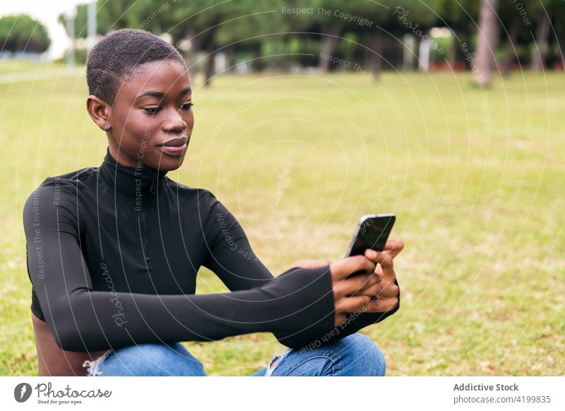 Charmante schwarze Frau mit Kopfhörern nimmt Selfie auf Smartphone Selbstportrait Afroamerikaner ethnisch Sitzen Gras Park charmant Porträt Funktelefon Foto