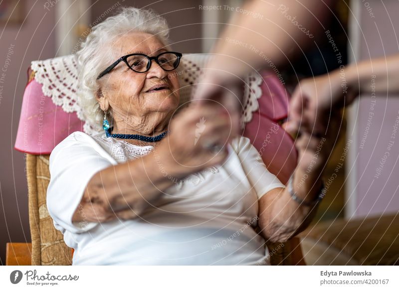 Weibliche Pflegekraft unterstützt alte Frau beim Aufstehen aus dem Sessel im Pflegeheim Menschen Senior reif lässig Kaukasier älter heimwärts Haus Alterung