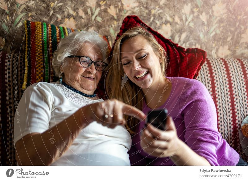 Ältere Frau und ihre erwachsene Enkelin nutzen gemeinsam ein Smartphone Menschen Senior reif lässig Kaukasier älter heimwärts Haus alt Alterung häusliches Leben