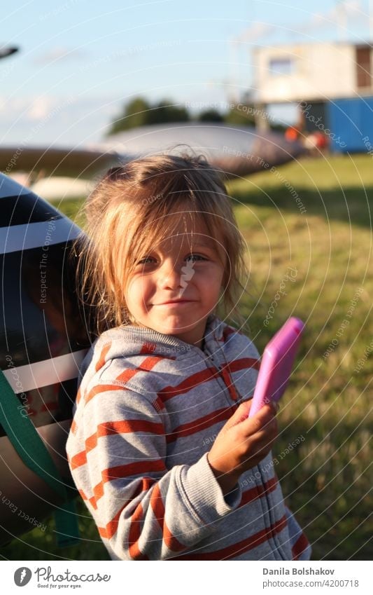 Kind spielt Fotograf im Freien. Mädchen stellt sich vor, Bilder auf rosa Plastikspielzeug Telefon zu nehmen Schönheit Lächeln Rasen Hobby Konzept genießen