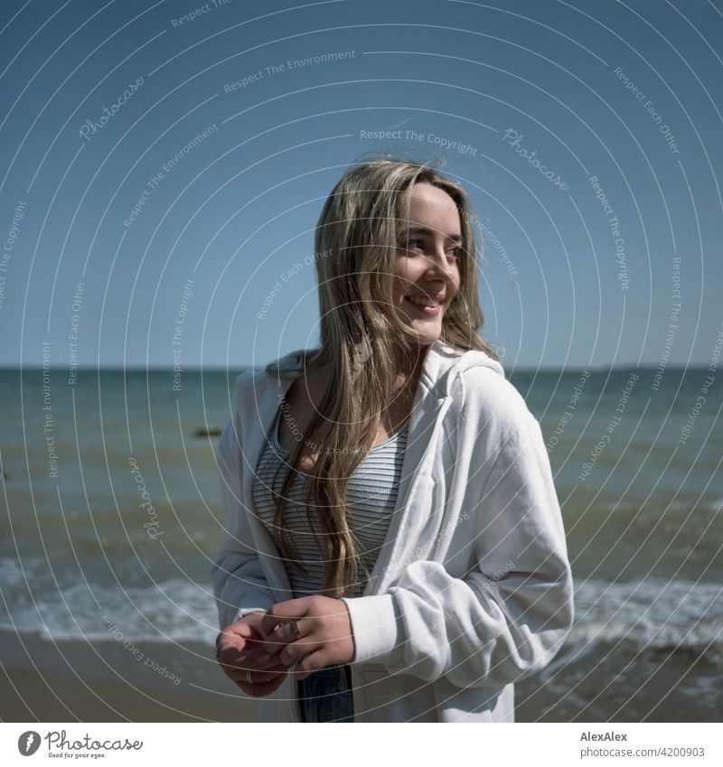 Analoges, rechteckiges Bild eines schönen blonden Mädchens das am Strand der Ostsee steht und  zur Seite schaut Lächeln freudig Landschaft durch Freude