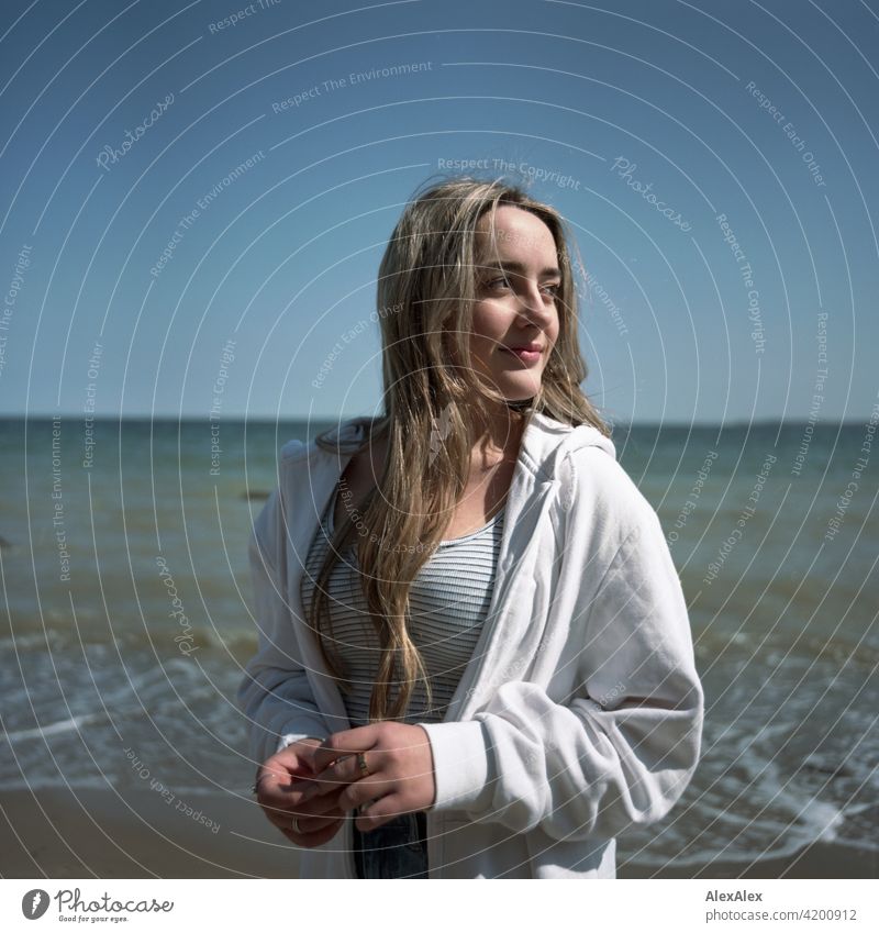 Analoges, rechteckiges Bild eines schönen blonden Mädchens das am Strand der Ostsee steht und  zur Seite schaut Lächeln freudig Landschaft durch Freude