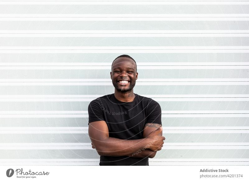 Fröhliches schwarzes Männchen in der Nähe der gestreiften Wand stehend Mann heiter herzlich Freundschaft Glück Porträt Streifen Inhalt froh männlich Lächeln