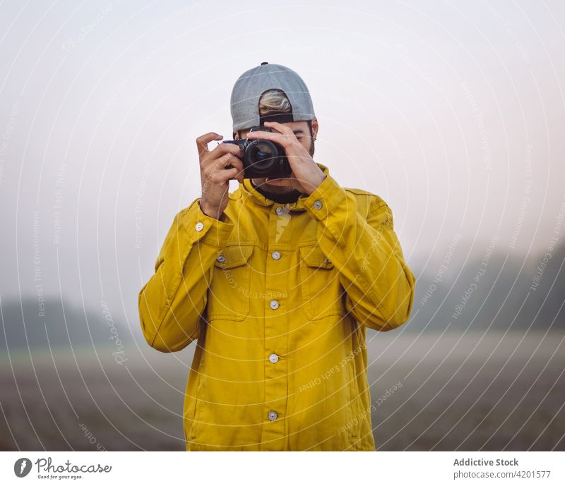 Mann nimmt Foto auf Kamera in nebliger Natur fotografieren Landschaft Nebel Fotografie Fotoapparat Wiese Jeansstoff Lifestyle Gerät Apparatur jung Mobile