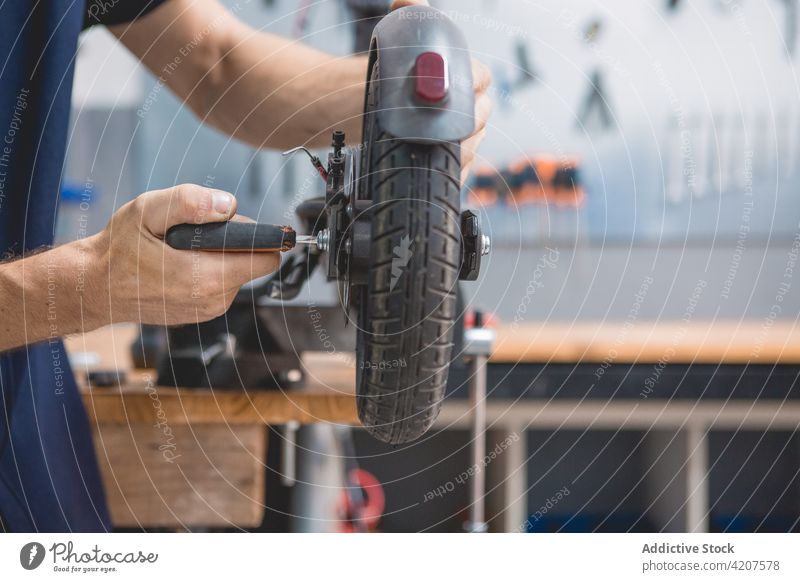 Mechaniker repariert das Rad eines Rollers in der Werkstatt Tretroller Reparatur fixieren Schraubendreher Mann Fahrzeug Dienst Werkzeug Techniker männlich