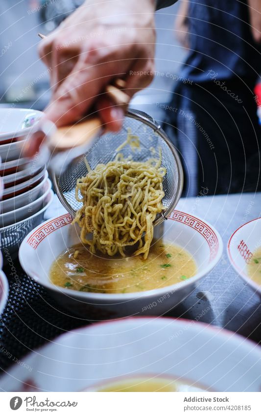 Zubereitung von Ramen-Suppe im Restaurant Küche Nudeln lecker Japanisches Essen Teller Sieb unerkannt Vorderansicht gesichtslos Gießen asiatisch Lebensmittel