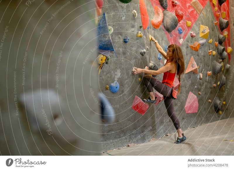 Aktive Frau klettert an der Wand im Fitnessstudio Sportlerin klettern Bouldern Fokus extrem Konzentration Stärke Training stark Bergsteiger aktiv sportlich