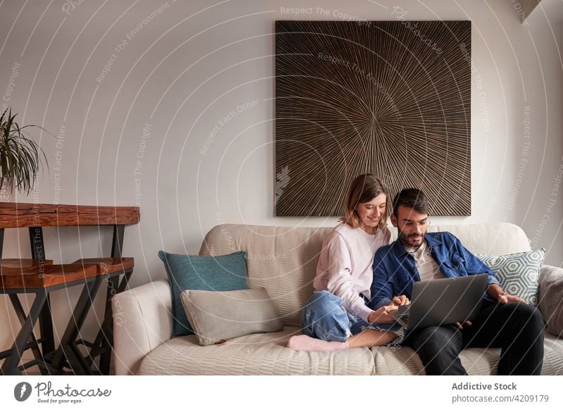 Lächelndes junges gemischtes Paar beim Video-Chat auf dem Netbook Gruß Gespräch Laptop heiter Zusammensein Sofa reden online Optimist Glück multiethnisch