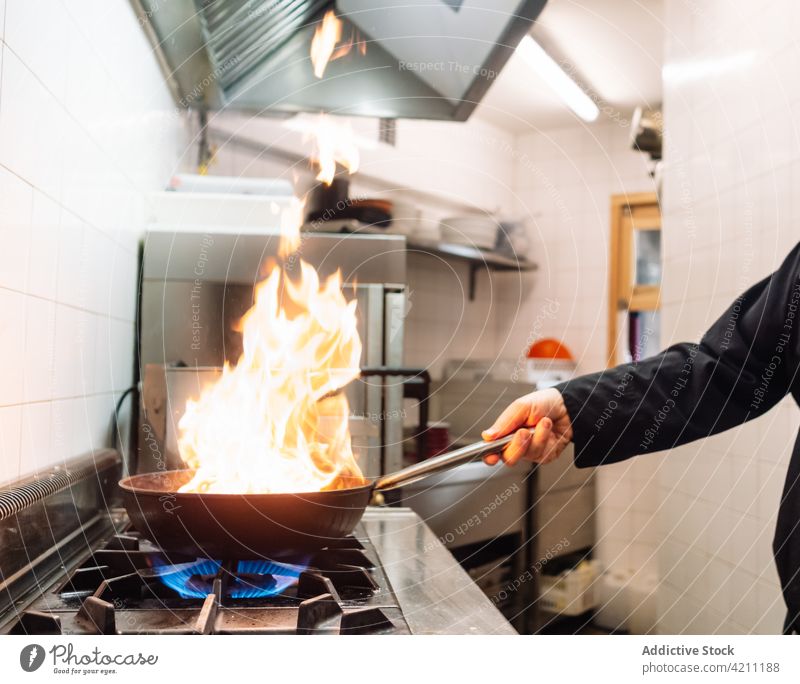 Crop-Koch bei der Zubereitung von Speisen auf Feuer in der Pfanne Küchenchef Flamme Herd braten Restaurant heiß Lebensmittel Mahlzeit vorbereiten Prozess