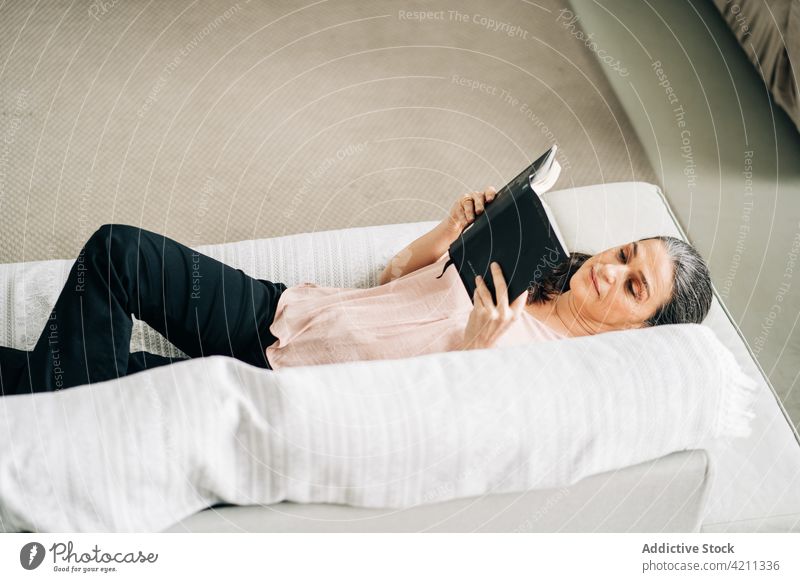 Konzentrierte Frau, die auf der Couch ein Buch liest lesen Liege Sofa Appartement heimisch Hobby Leseratte Wohnzimmer liegend heimwärts lässig Konzentration