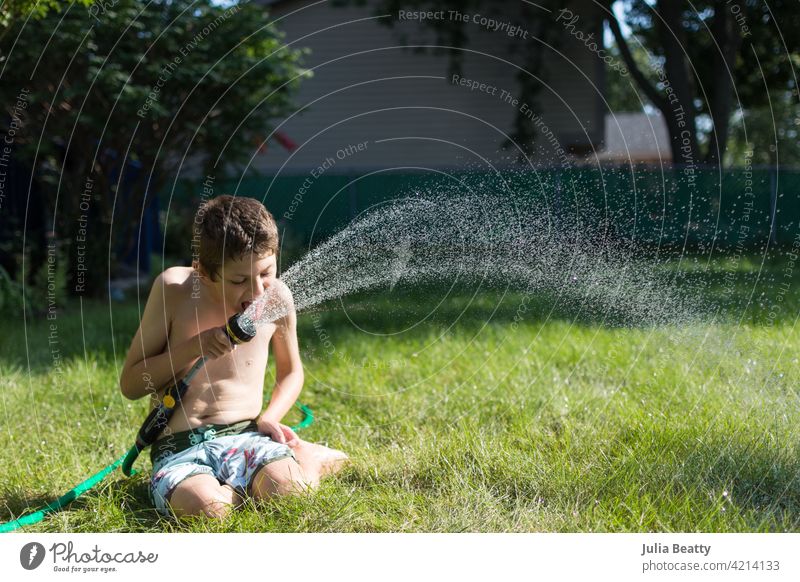 Junge mit Autismus spielt mit Gartenschlauch in seinem Hinterhof; Sommerzeit im Mittleren Westen der USA Schlauch Spray spielen trinken sensorisch