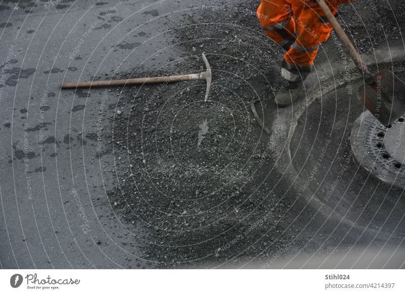 Straßenbauarbeiter mit orangener Hose und Schaufel strassenarbeiter schaufel hose reflektierend arbeiten stemmarbeiten kanaldeckel manhole asphaltarbeiten