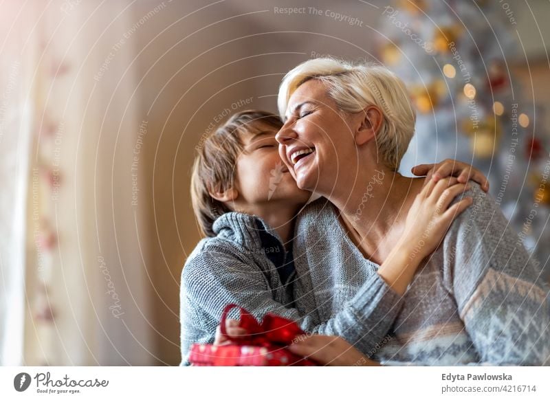 Sohn gibt Mutter Weihnachtsgeschenk Junge Kind Kinder umarmend Winter Weihnachten Weihnachtsbaum Lifestyle im Innenbereich Glück Menschen Kaukasier Spaß Freude