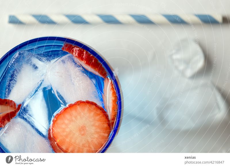 Aromatisches frisches Wasser mit Erdbeere und Eiswürfel, Trinkhalm liegt bereit Getränk Erfrischungsgetränk Obst Frucht kalt erfrischend blau rot weiß Glas rund
